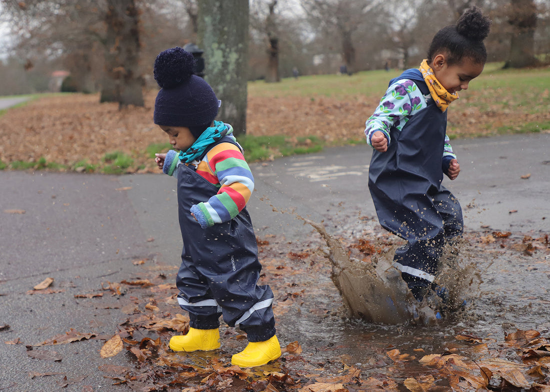 School and nursery children wearing waterproof dungarees and splashing in puddles