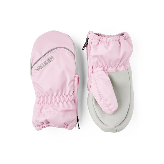 A pair of children's mittens in light pink and light gray, shown from both the back and front views on a clean white background. The back view shows a gray reflective stripe and the brand name 'HESTRA' printed in gray.