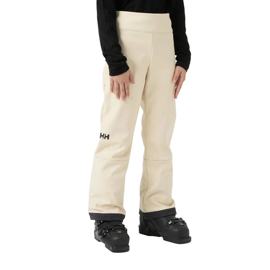 A person wearing cream-colored Helly Hansen snow pants with a black long-sleeve top and black ski boots, shown from the waist down on a white studio background.