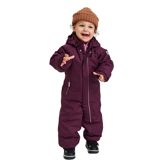 A toddler wearing a dark purple hooded snowsuit, a brown knit beanie, and black shoes, standing against a light gray studio background.