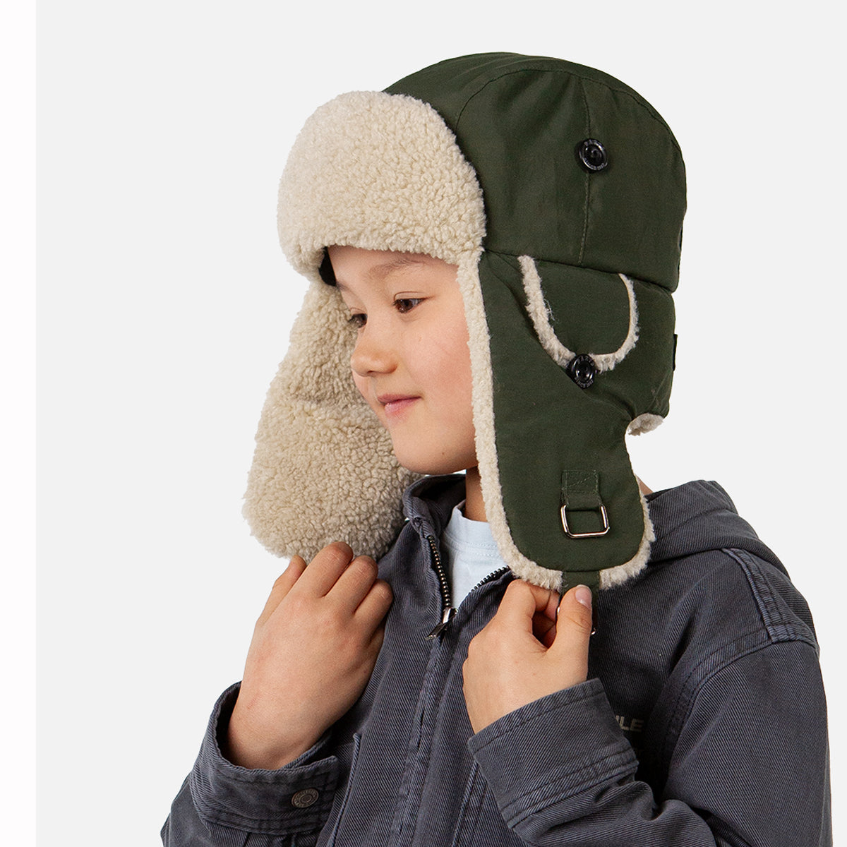 Child wearing a green winter hat with beige earflaps on a white background