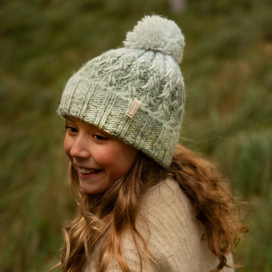 Child wearing a green knitted hat with a pom-pom in a natural setting