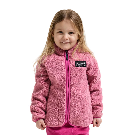 A young girl with blonde hair wearing a pink sherpa fleece zip-up jacket with a black logo patch on the chest, photographed against a light gray studio background.