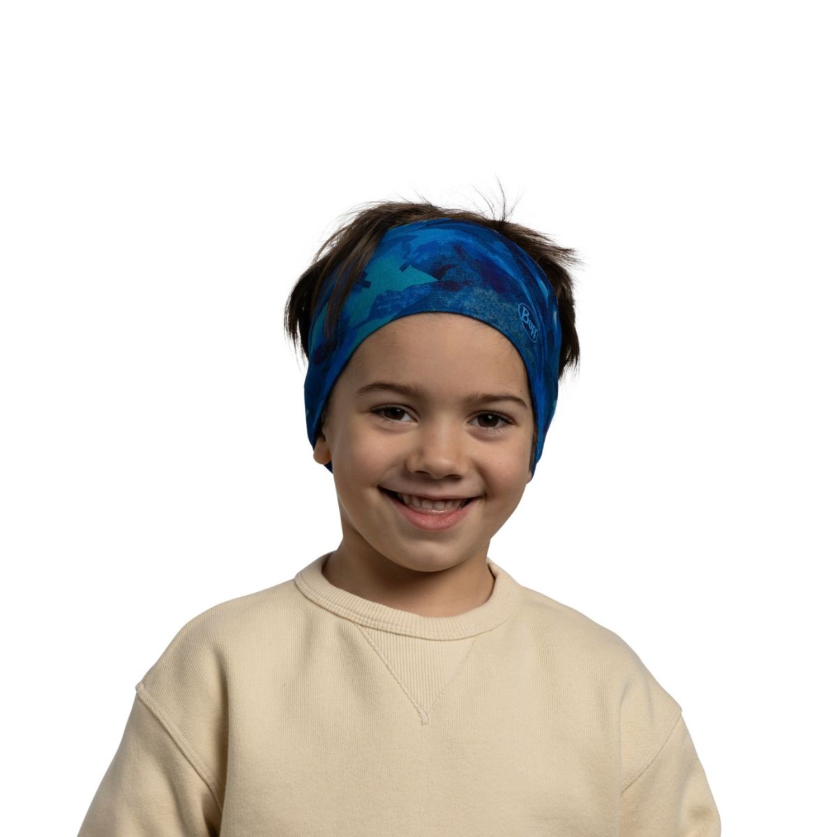 A smiling young child wearing a blue patterned headband and a cream sweatshirt, photographed against a plain white background.