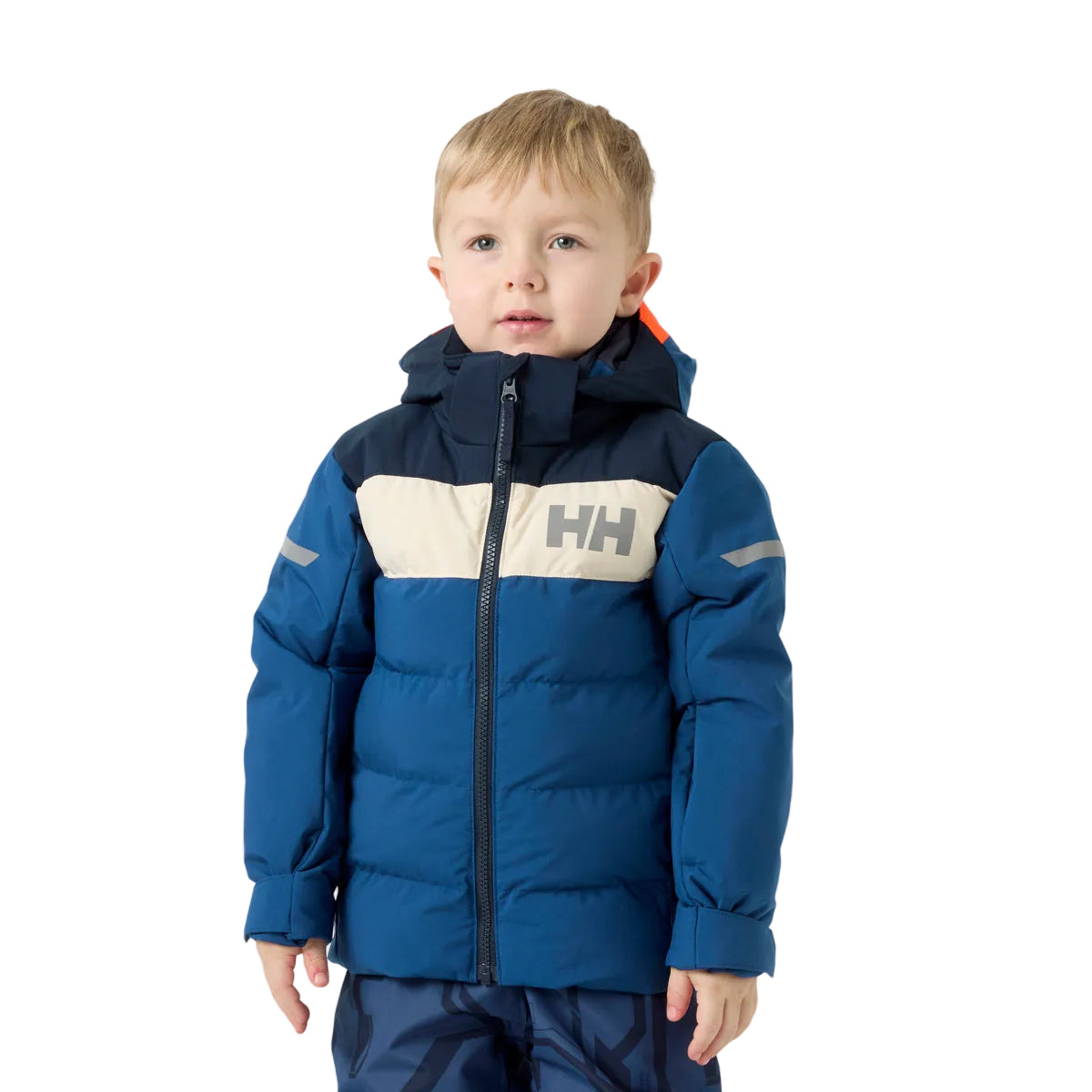 A young boy wearing a blue and navy puffer jacket with a beige chest panel and the Helly Hansen 'HH' logo, paired with dark patterned pants, against a light gray studio background.