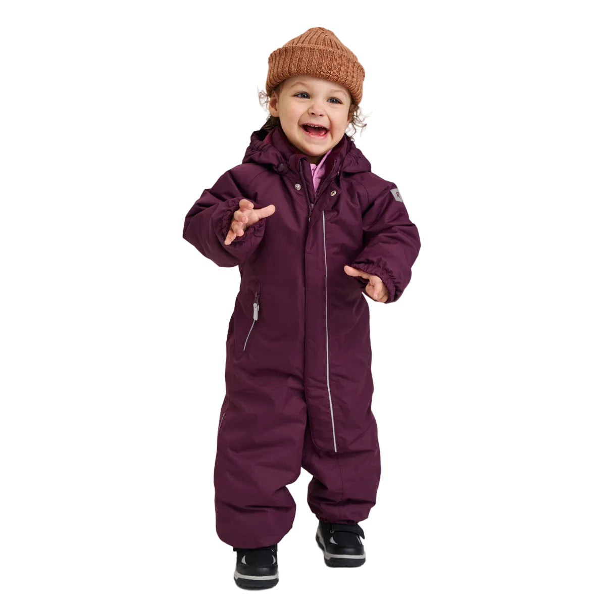 A toddler wearing a dark purple hooded snowsuit, a brown knit beanie, and black shoes, standing against a light gray studio background.