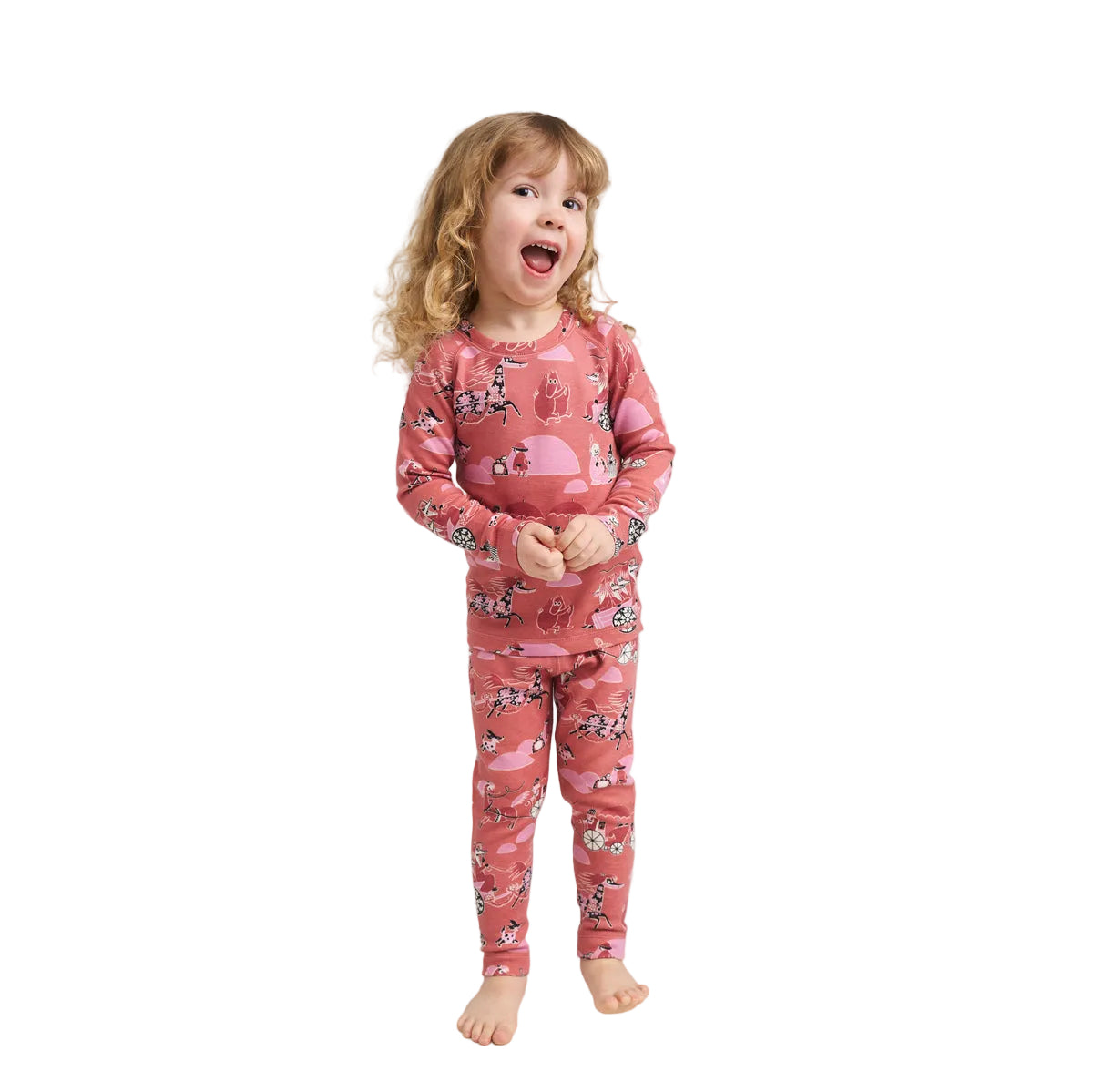 A young child with curly blonde hair stands barefoot against a light gray studio background, wearing a long-sleeve and matching one-piece pajama set in dusty pink with a cartoon animal print.