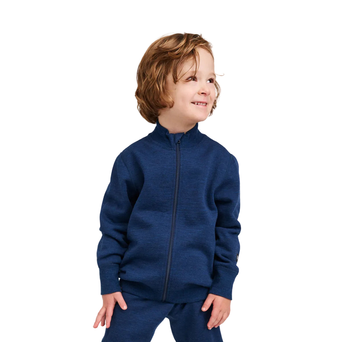 A young child with wavy light brown hair wearing a navy blue zip-up fleece jacket and matching navy pants, standing against a light gray studio background.
