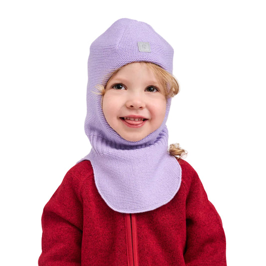 A smiling young child wearing a light purple knit balaclava hood and matching neck gaiter over a red fleece jacket, photographed against a clean light gray studio background.