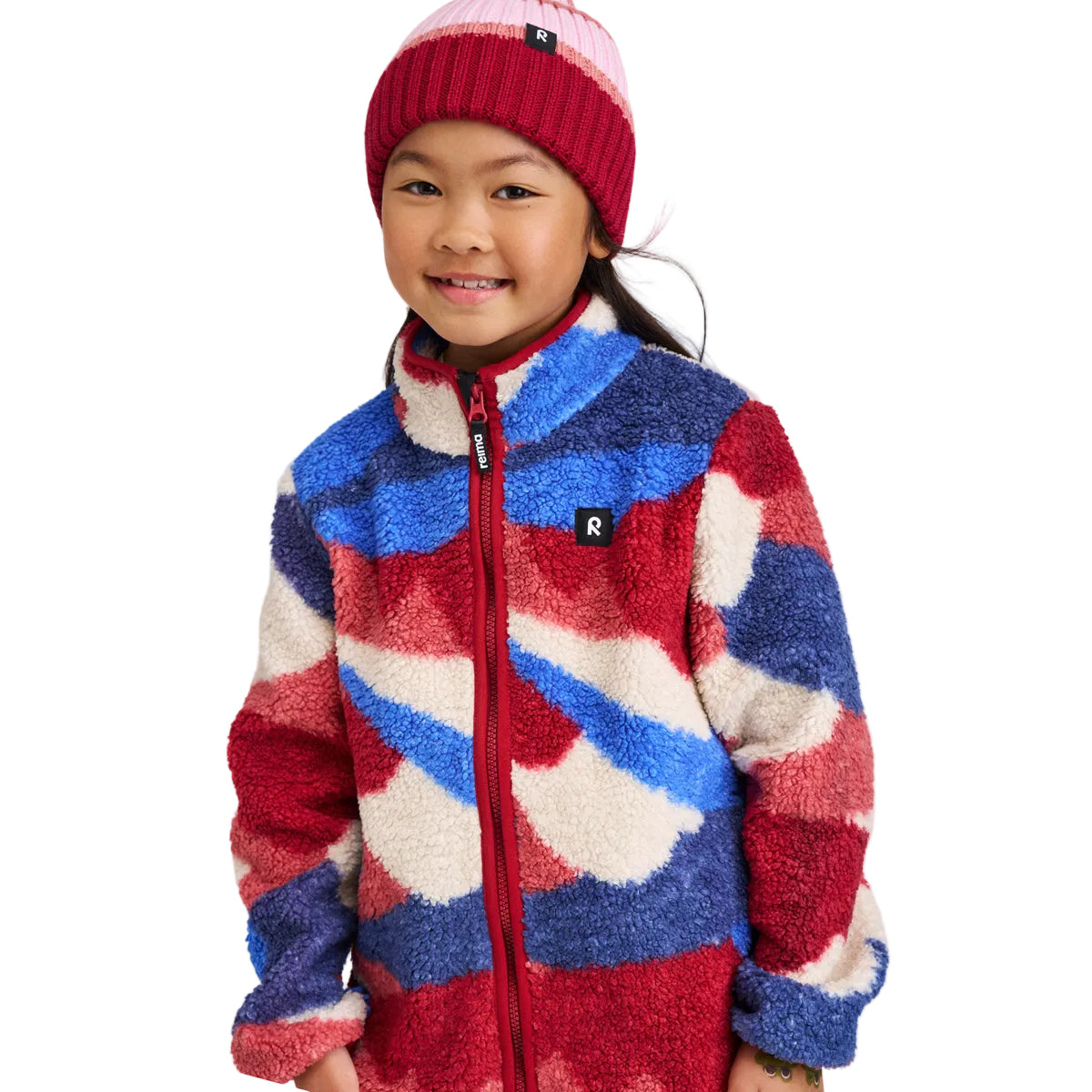Child wearing a colorful patterned jacket and red knit hat on a white background