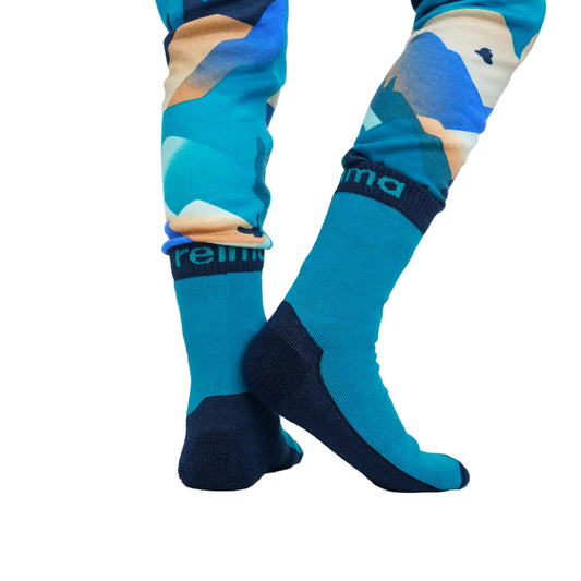 A close-up of a kid's legs wearing colourful socks with a blue, teal, and beige mountain pattern and dark navy heels, toes, and cuffs.