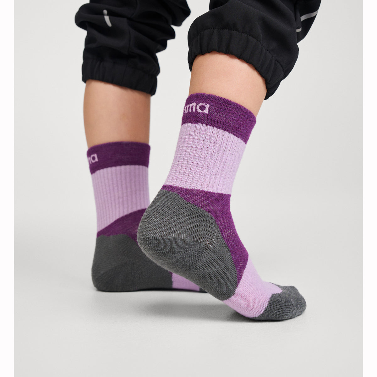 Purple and gray socks with brand logo worn by a child on a light gray background