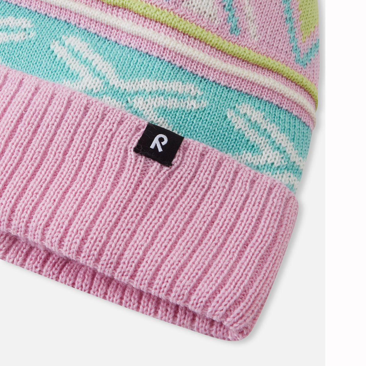Close-up of a knit beanie with a pink ribbed cuff, a turquoise and white patterned band, and a small black square logo patch with a white letter R.