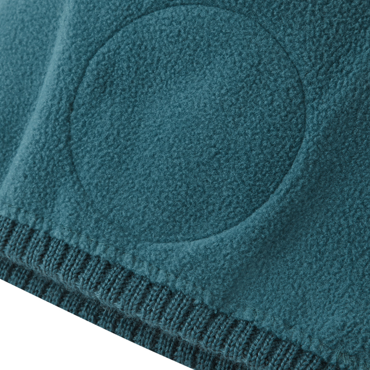 Close-up of a teal fleece blanket with a ribbed knit edge and a circular tufted detail.