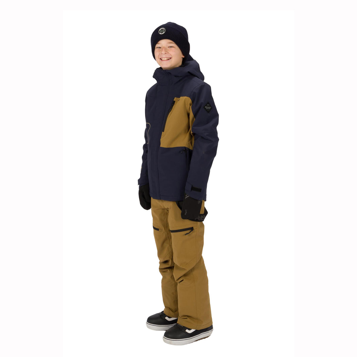 A child wearing a dark navy and tan snowboard jacket, matching tan snow pants, a black beanie, and black skate shoes, standing against a plain white background.