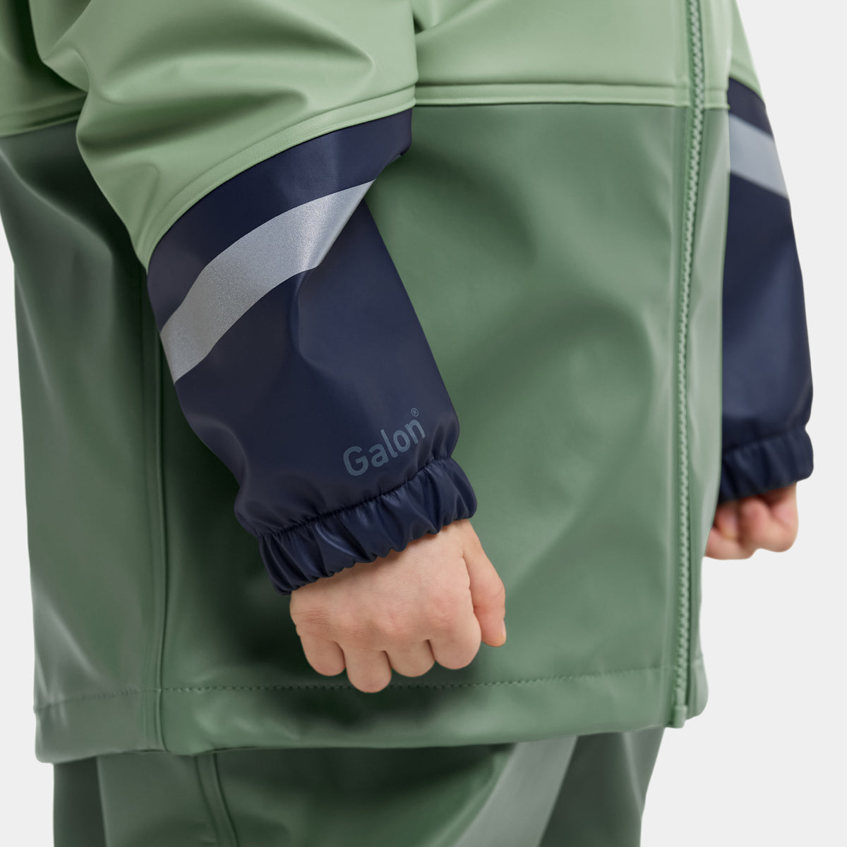 Close-up of a child wearing a green and navy waterproof jacket, showing the sleeve with a reflective silver stripe and the brand name 'Galoni' printed on the cuff.