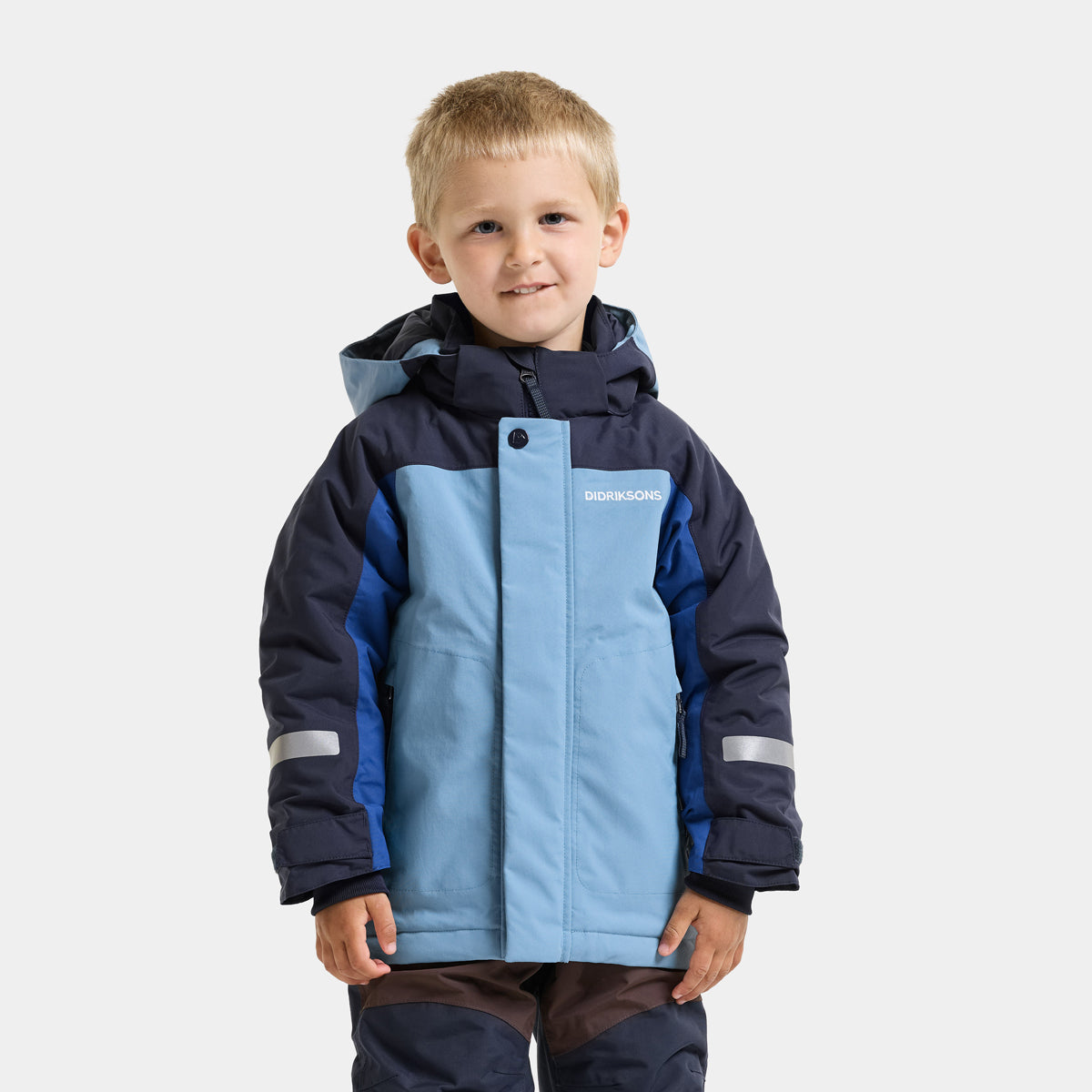 A young boy wearing a hooded winter jacket in light blue and navy blue, with reflective silver stripes on the sleeves, standing against a light gray background.