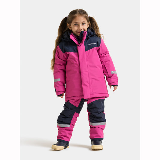 A young girl wearing a bright pink and navy blue winter snowsuit with reflective silver stripes, standing against a light gray studio background.