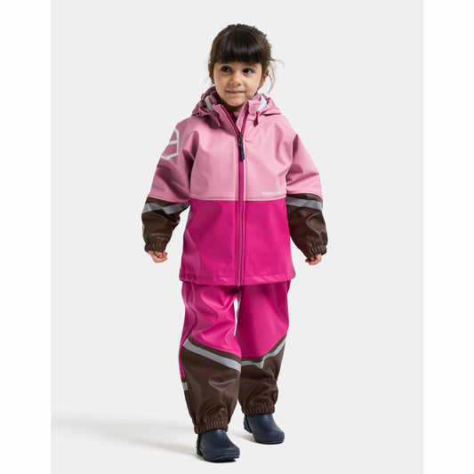 A young child wearing a two-piece waterproof rain suit in pink and magenta with brown and gray accents, standing against a light gray studio background.