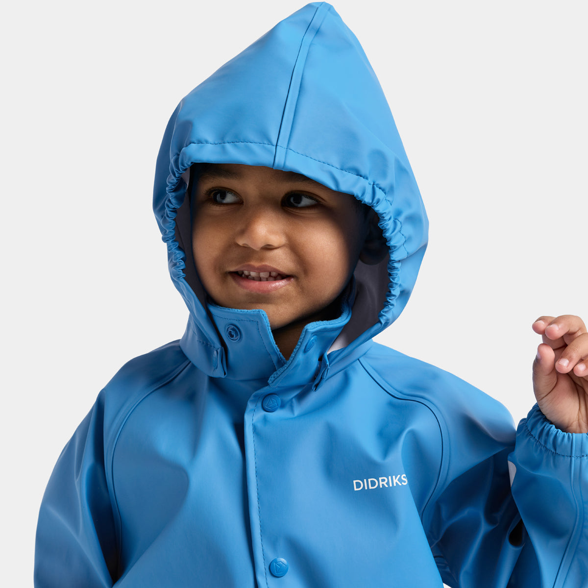 A young child wearing a bright blue hooded rain jacket with the brand name 'DIDRIKSONS' printed on the chest, photographed against a clean light gray background.
