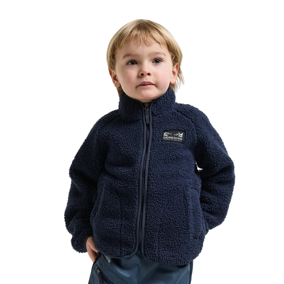 A young child wearing a navy blue sherpa fleece zip-up jacket with a small black and white Patagonia logo patch on the left chest, photographed against a light gray studio background.