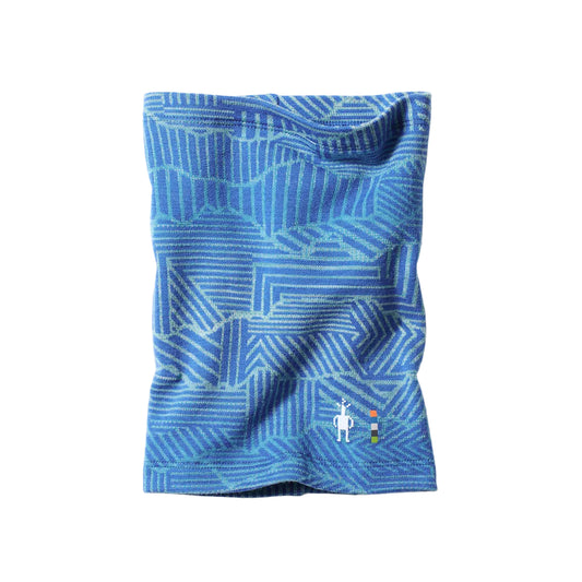 A blue patterned kids neck gaiter or balaclava with a geometric design, featuring a small white logo near the bottom right, displayed on a light gray background.