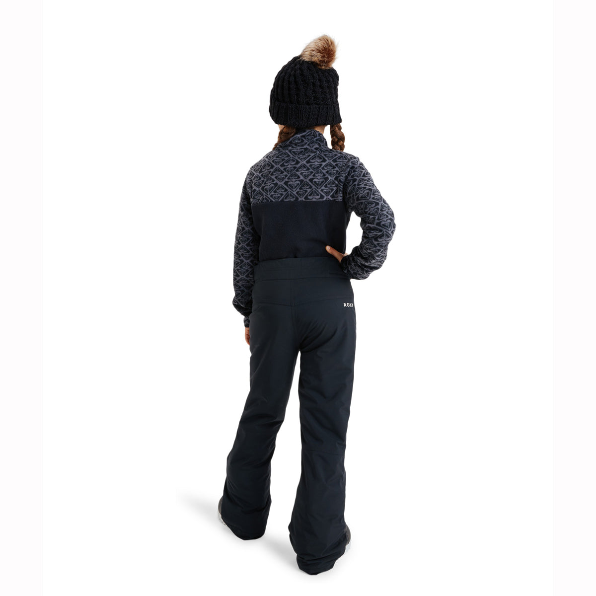 A child shown from the back wearing a dark navy ski jacket with a patterned yoke and matching dark pants, along with a black knit beanie with a brown pom-pom, on a white studio background.
